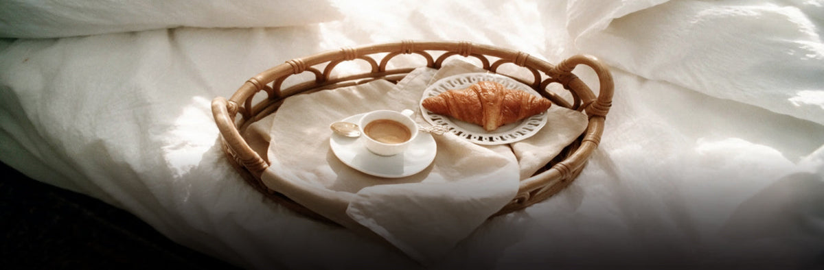 Vanilla menu photo of coffee and a croissant on a rattan tray over white bedding
