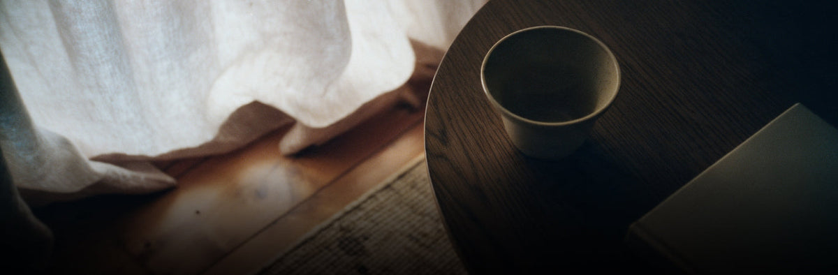 Woody menu photo of a cup on a dark wood table beside a linen curtain