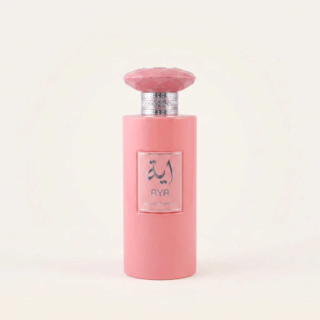 AYA Eau de Parfum cylindrical opaque pastel pink bottle topped with a matching faceted gem-shaped cap and textured silver collar, featuring a square silver-framed label with metallic silver Arabic calligraphy.