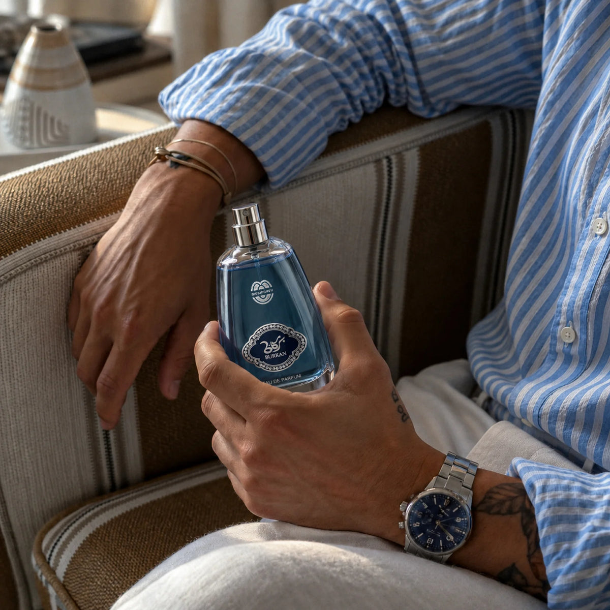 Burkan for men perfume bottle held by a seated man in a striped shirt