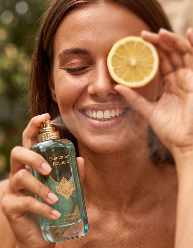MUSHMUSH Glamorous Bouquet women perfume, 100ml Eau de Parfum, affordable luxury fragrance with fresh lemon citrus notes, shown being sprayed by a woman holding a lemon outdoors.