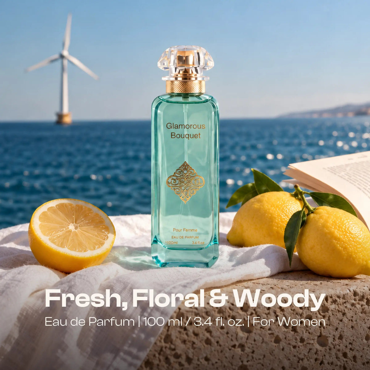 Glamorous Bouquet Pour Femme bottle by the sea with lemons, an open book and a distant wind turbine